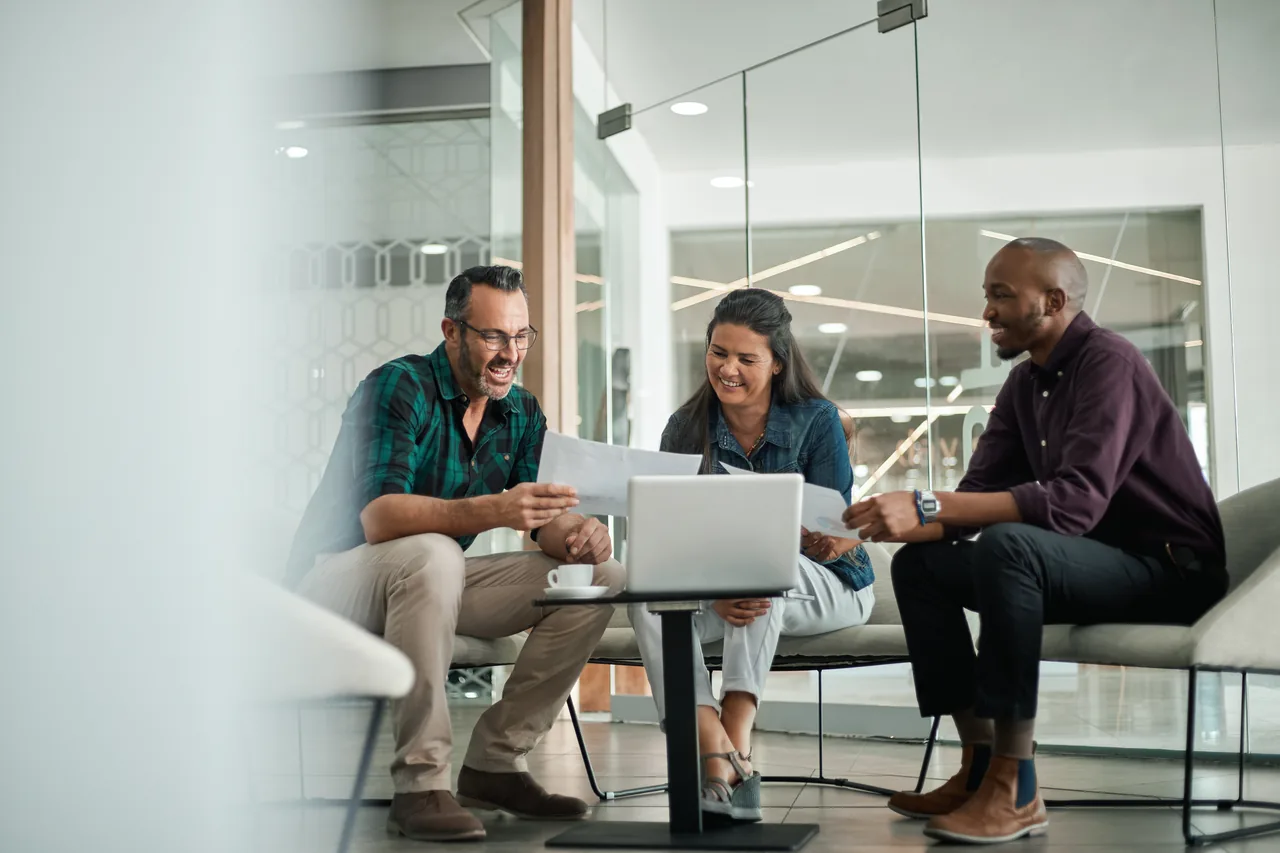 Three colleagues discussing documents around a laptop