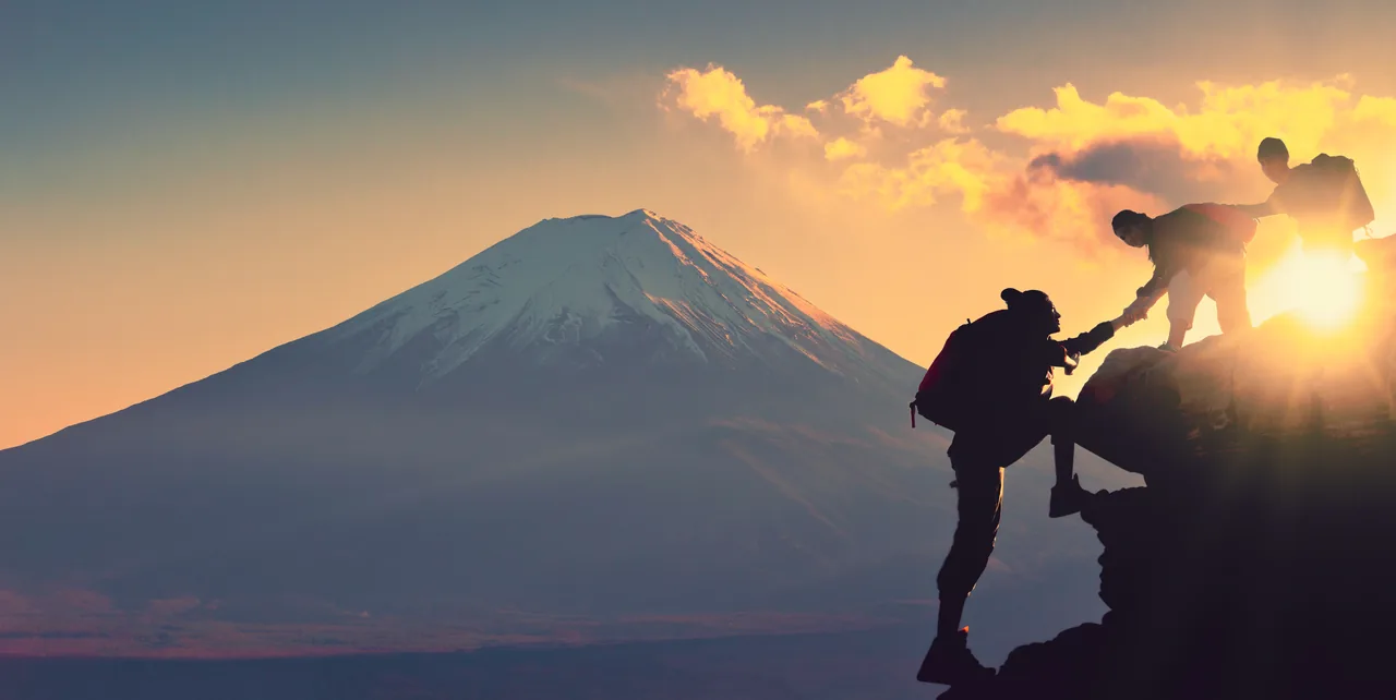 Hikers helping one another climb a rocky ledge at sunset