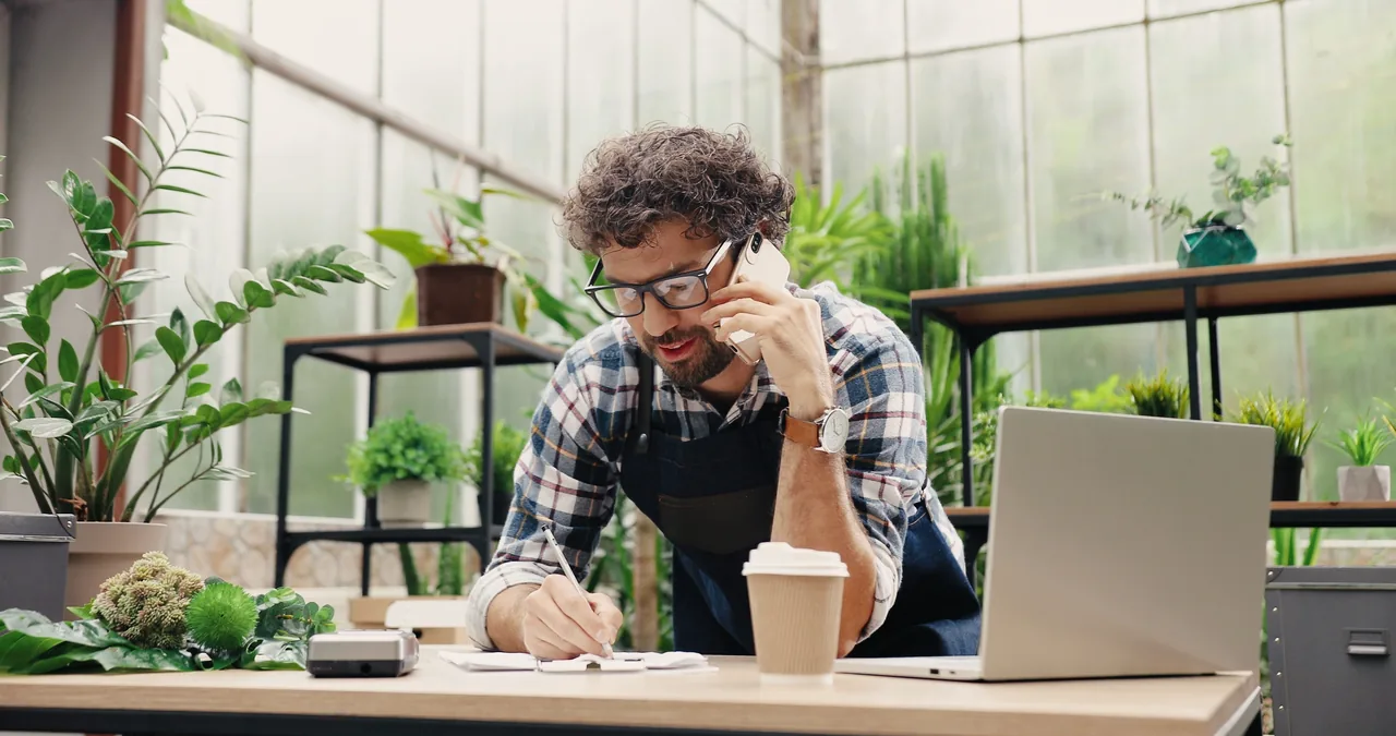 A shop owner taking a call and making notes among plants